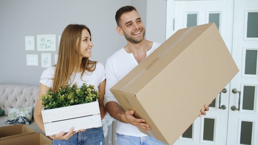 Couple carrying moving boxes and a plant into a new home